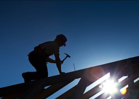 Lone roofer hammering at sundown